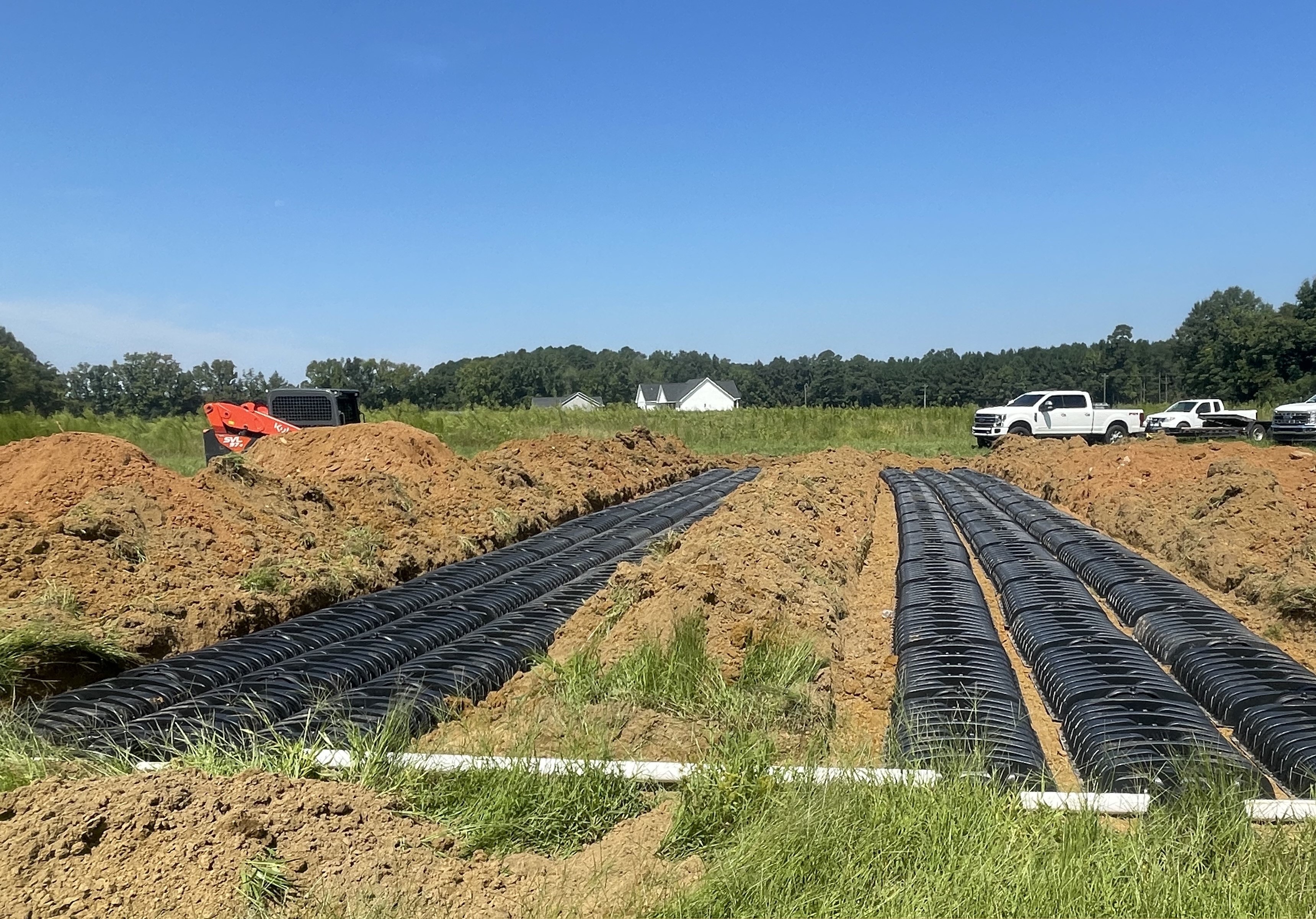 Rows of black drainage chambers installed in a dug-out field with trucks and equipment nearby.