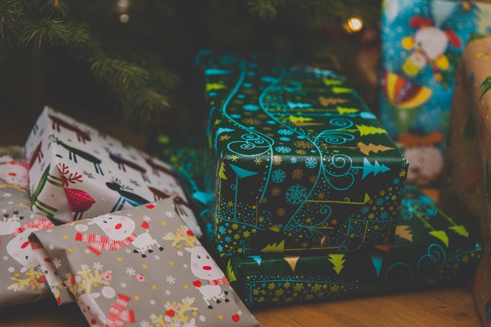 Stacks of colorful Christmas gifts with festive wrapping, featuring snowflakes, reindeer, and Santa motifs, placed under a decorated tree. 