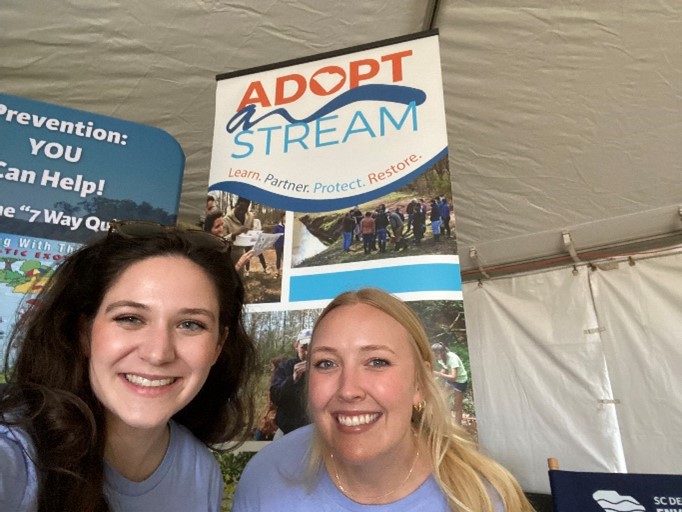 two people pose in front of an adopt a stream pop up banner