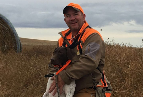 Portrait of Chris Corley in a high visibility vest with a pointer breed dog