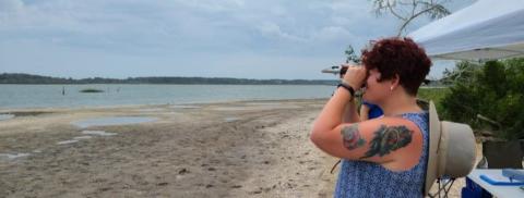 person standing on beach looking through binoculars