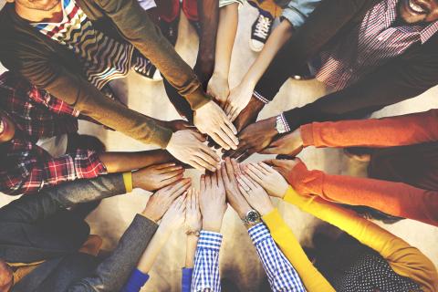 Overhead view of multiple people joining hands in a circle, symbolizing teamwork and unity.