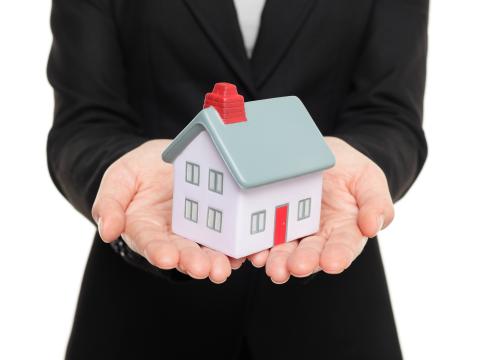 A person in a suit holds a small model house in both hands.